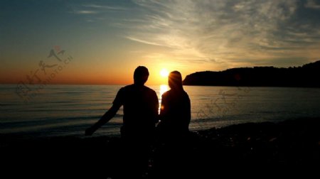 日落时分并肩坐在海滩边的浪漫恋人