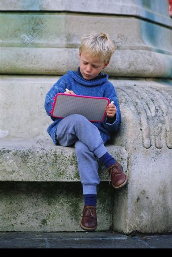 石柱旁坐着写字的外国男孩图片