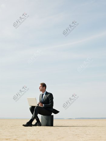 坐在箱子上操作电脑的外国男人图片