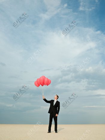 蓝天下拿着一把红气球的外国男人图片
